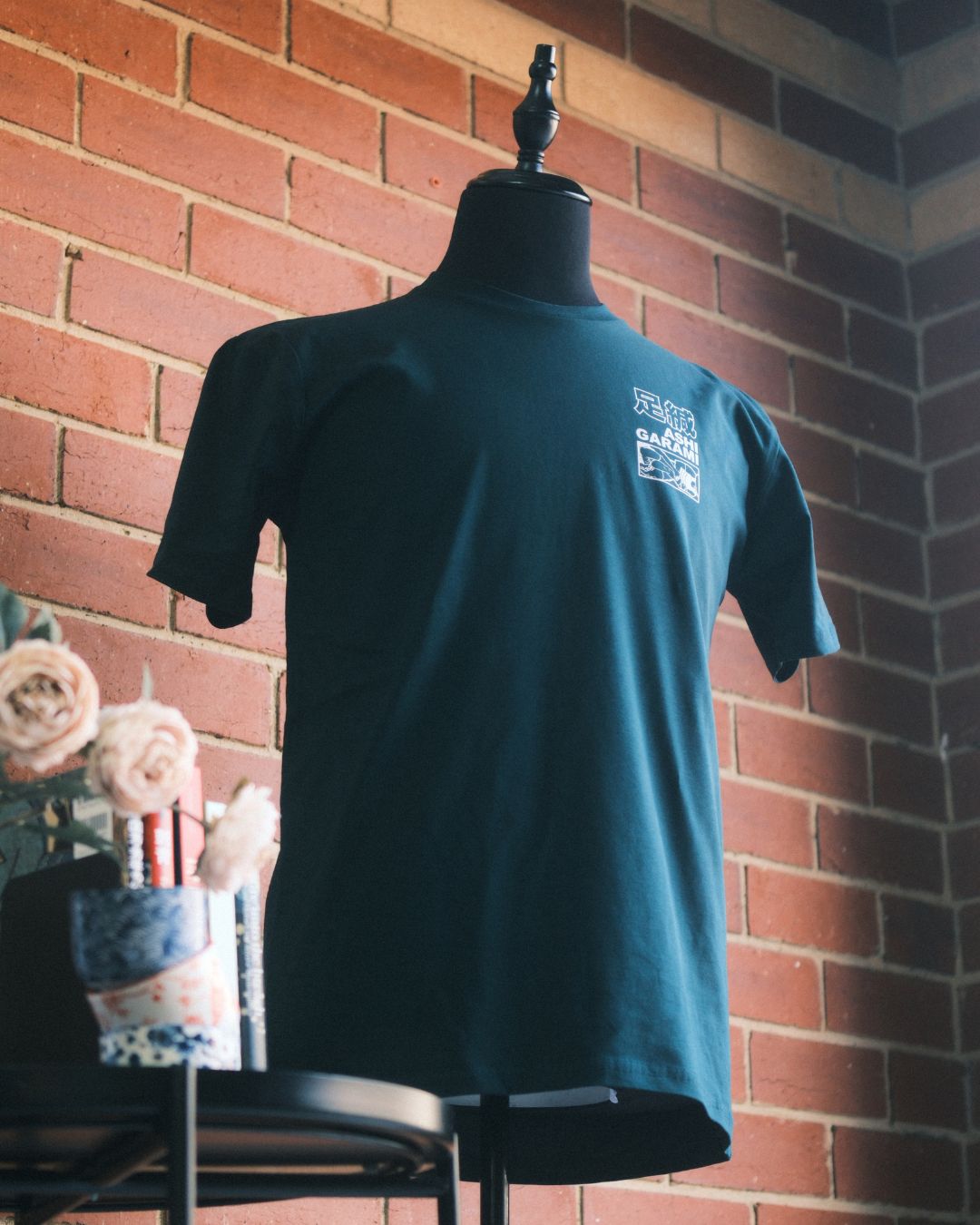 Green t-shirt with white graphics and text on the back, hanging against a brick wall. with ashi garami, leg entanglement graphic for artwork licensing on tshirt
